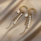 Flat-lay of gold bamboo hoop earrings with dangling baroque pearls and delicate metal chains