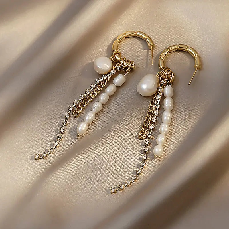 Flat-lay of gold bamboo hoop earrings with dangling baroque pearls and delicate metal chains