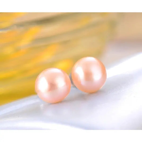 Delicate peach-colored freshwater pearl stud earrings resting on a smooth reflective surface