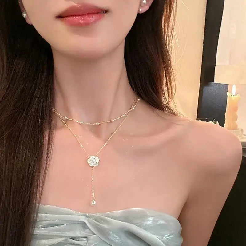 Layered gold-tone chain necklace with small pearls and a white rose charm