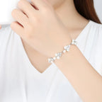 Dainty silver-toned leaf and flower pearl bracelet worn on wrist against a white top