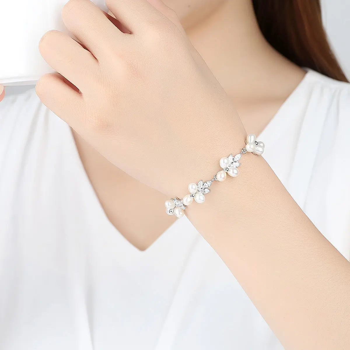 Dainty silver-toned leaf and flower pearl bracelet worn on wrist against a white top