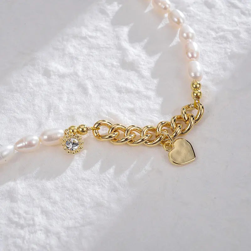 Close-up of asymmetrical pearl and gold chain necklace with sunburst and heart pendants
