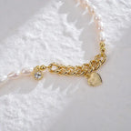 Close-up of asymmetrical pearl and gold chain necklace with sunburst and heart pendants