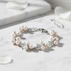 Elegant silver pearl bracelet in a circle shape on white marble surface with scattered petals