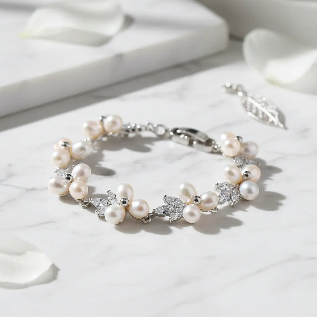Elegant silver pearl bracelet in a circle shape on white marble surface with scattered petals