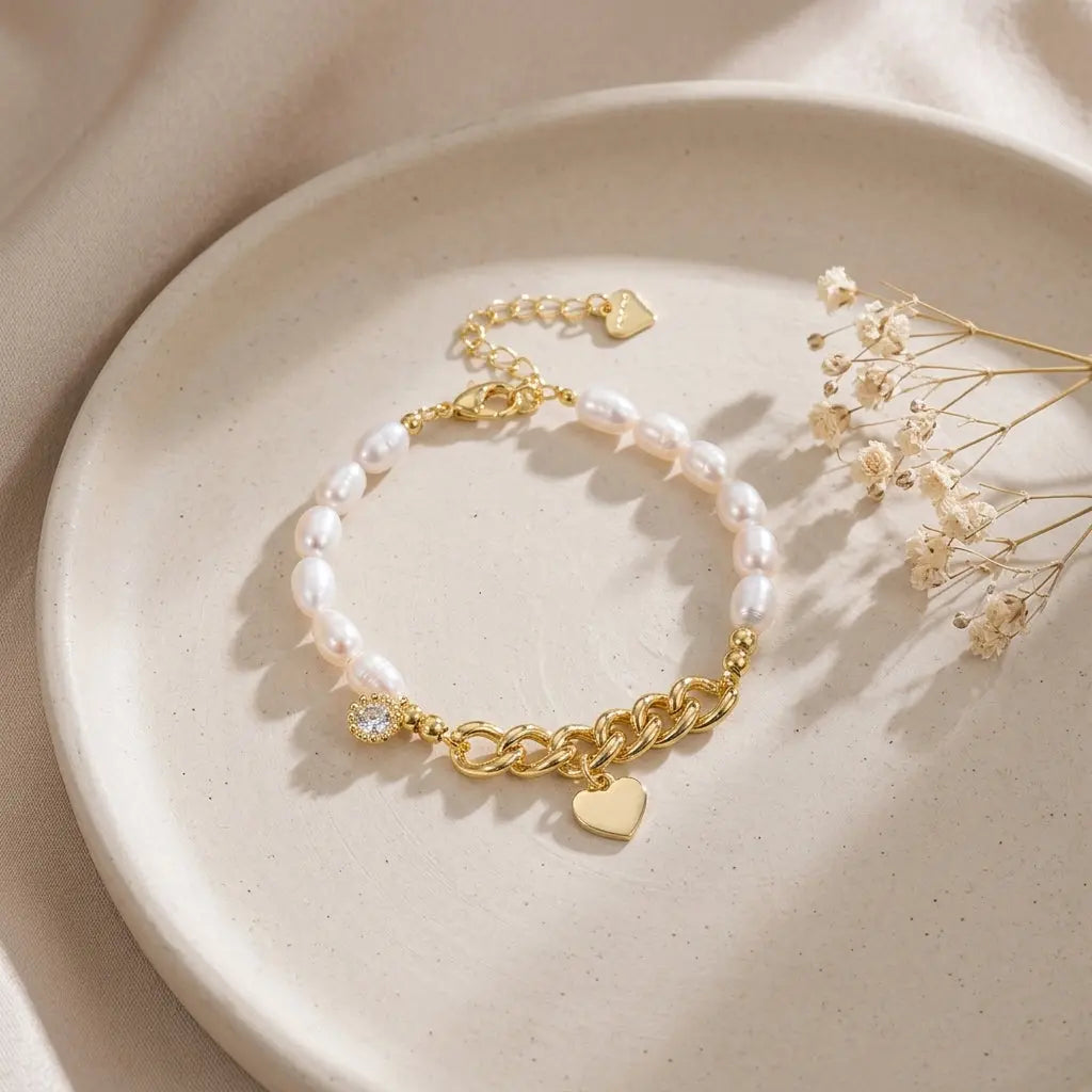 Asymmetrical gold link and freshwater pearl bracelet with heart charm on a ceramic tray