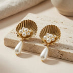 Gold Scallop Shell Pearl Drop Earrings on a minimalist travertine stone platform